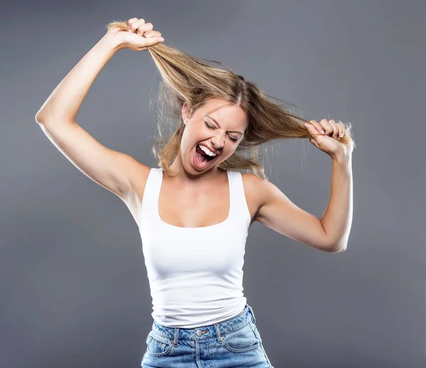 Schöne junge Frau zieht ihr Haar über grauen Hintergrund. — Stockfoto