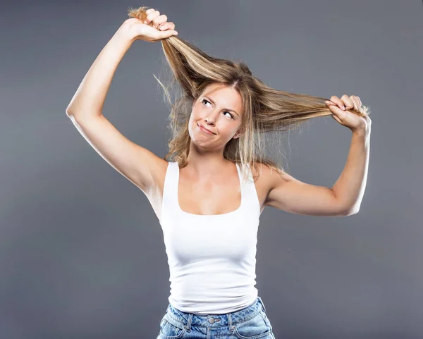 Mooie jonge vrouw haar haren trekken over grijze achtergrond. — Stockfoto