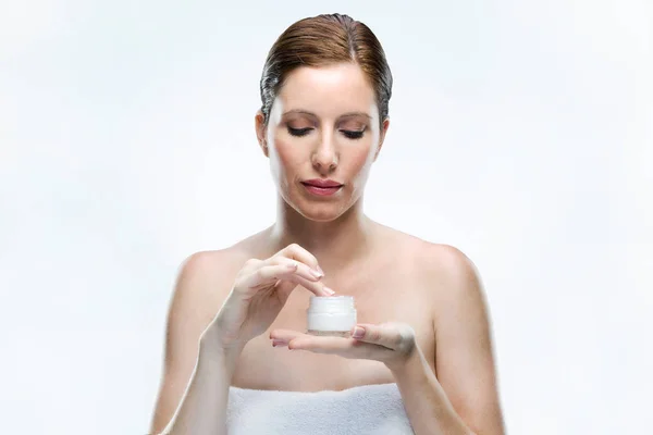 Beautiful young woman applying cosmetic cream on face over white background. — Stock Photo, Image