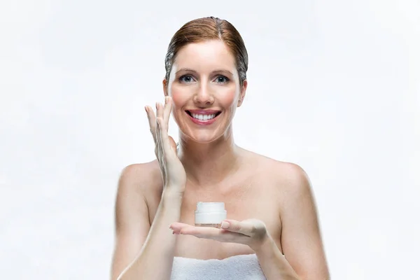 Beautiful young woman applying cosmetic cream on face over white background. — Stock Photo, Image