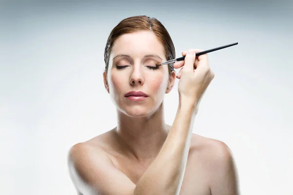 Mulher bonita aplicando maquiagem sobre fundo branco . — Fotografia de Stock