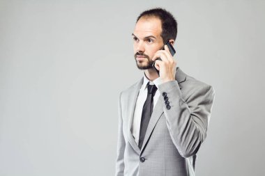 Onun cep telefonu gri arka plan üzerinde kullanan iş genç adam.