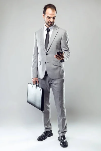 Jovem de negócios usando seu telefone celular sobre fundo cinza . — Fotografia de Stock