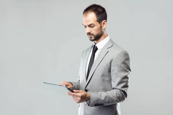 Jovem de negócios usando seu tablet digital sobre fundo cinza — Fotografia de Stock