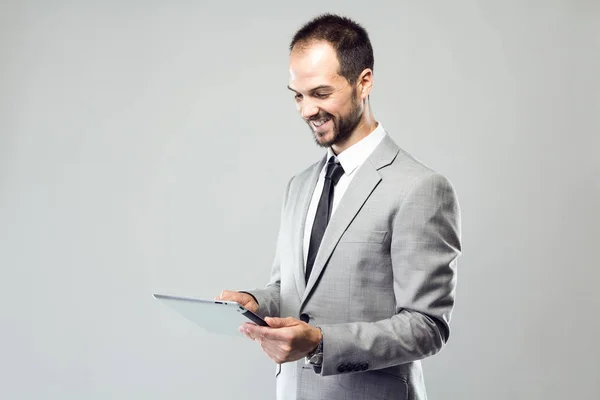 Jovem de negócios usando seu tablet digital sobre fundo cinza — Fotografia de Stock