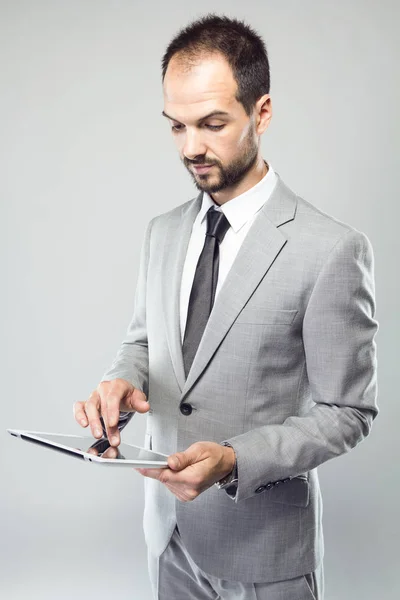 Hombre joven de negocios utilizando su tableta digital sobre fondo gris —  Fotos de Stock