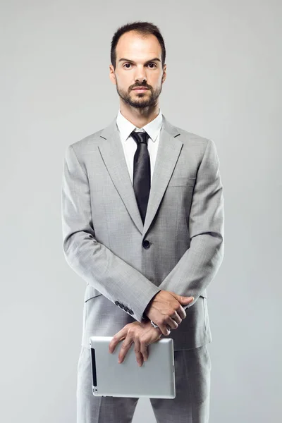 Hombre joven de negocios mirando a la cámara sobre fondo gris . — Foto de Stock