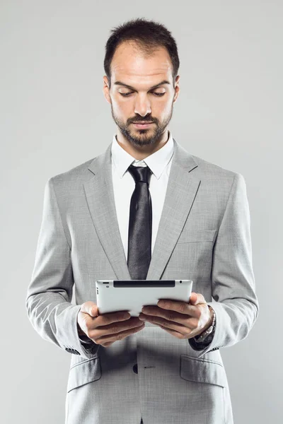 Hombre joven de negocios utilizando su tableta digital sobre fondo gris —  Fotos de Stock