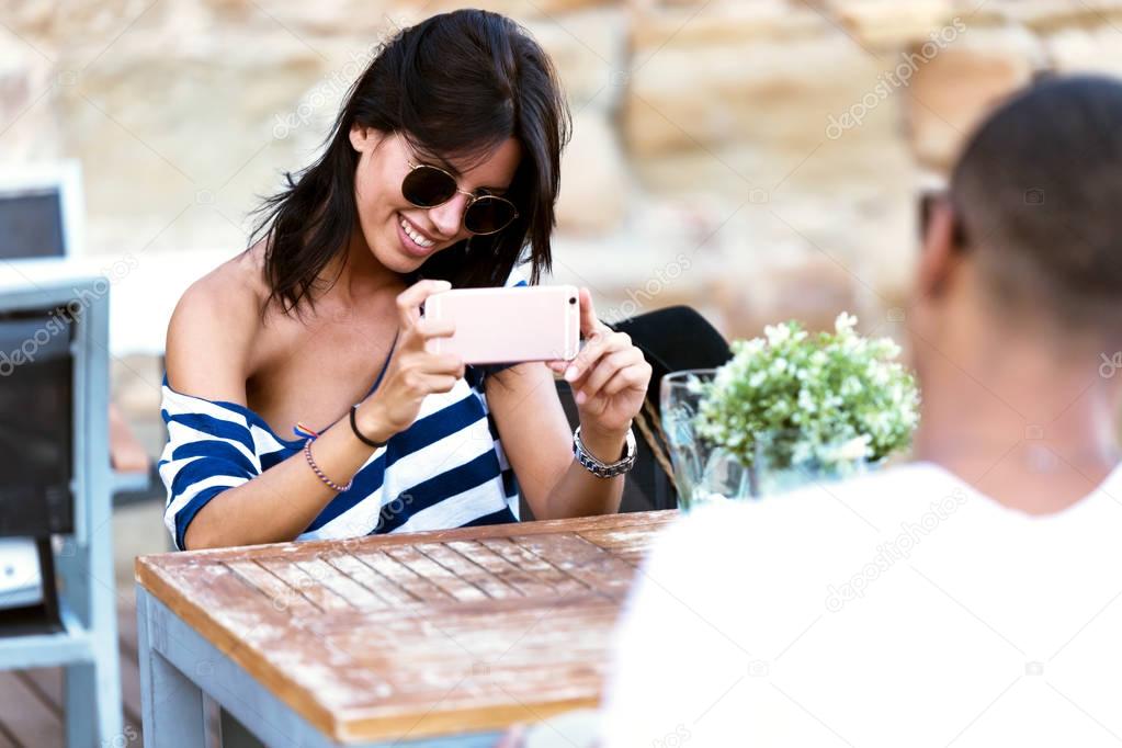 Beautiful young woman taking photo of her boyfriend in the stree