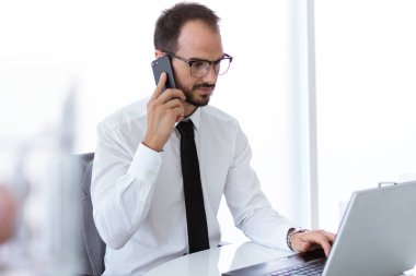 Dizüstü bilgisayar ve cep telefonu ofisteki çalımakta yakışıklı genç.