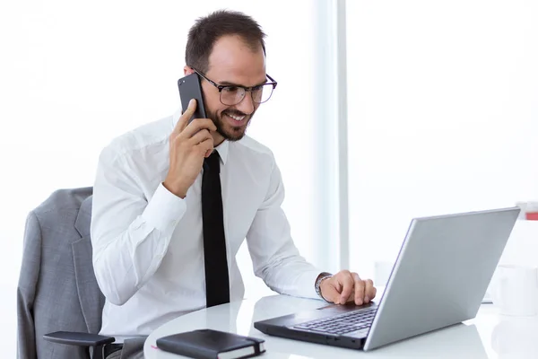 Jovem bonito trabalhando com laptop e telefone celular no escritório . — Fotografia de Stock