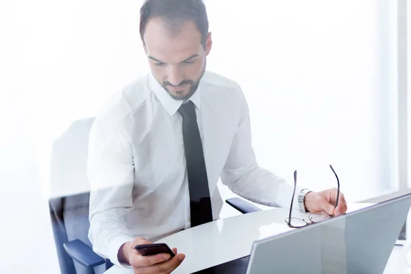 Stilig ung man arbetar med laptop och mobiltelefon på kontoret. — Stockfoto