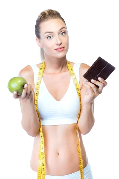 Schöne junge Frau hält einen Schokoriegel und einen Apfel vor weißem Hintergrund. — Stockfoto