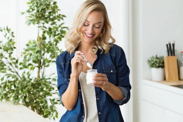 Hermosa mujer joven comiendo yogur en casa . — Foto de Stock