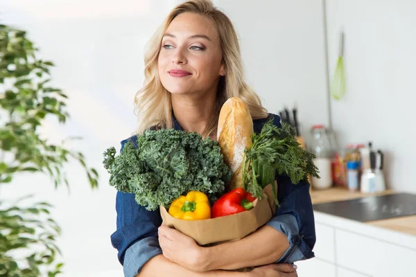 Vacker ung kvinna livsmedelsbutiker shoppingväska med grönsaker hemma. — Stockfoto