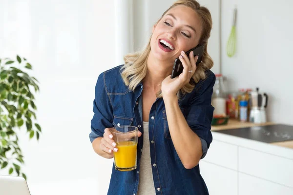 Vacker ung kvinna använder sin mobiltelefon i köket. — Stockfoto