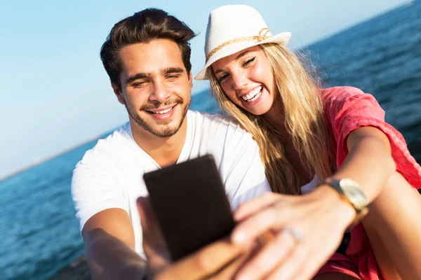 Beautiful young couple using mobile phone on the beach. — Stock Photo, Image