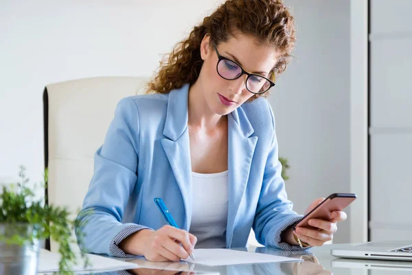 Vacker ung affärskvinna med hennes mobiltelefon på kontoret. — Stockfoto