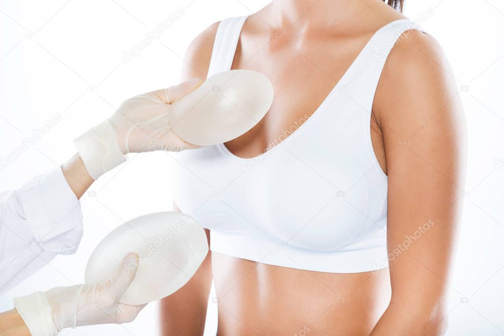 Female doctor choosing mammary prosthesis with her patient over white background.