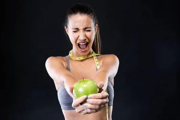 Wütende junge Frau mit Maßband um den Hals und einem Apfel vor schwarzem Hintergrund. — Stockfoto