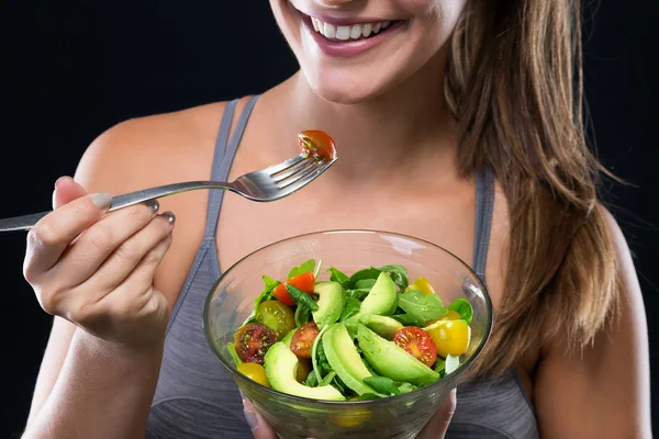 Schöne junge Frau isst Salat vor schwarzem Hintergrund. — Stockfoto