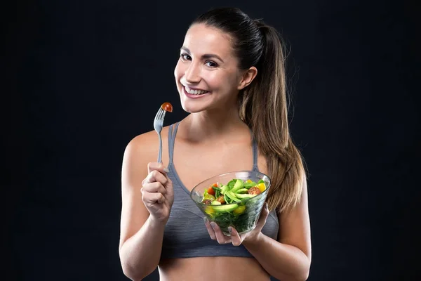 Hermosa mujer joven comiendo ensalada sobre fondo negro . —  Fotos de Stock