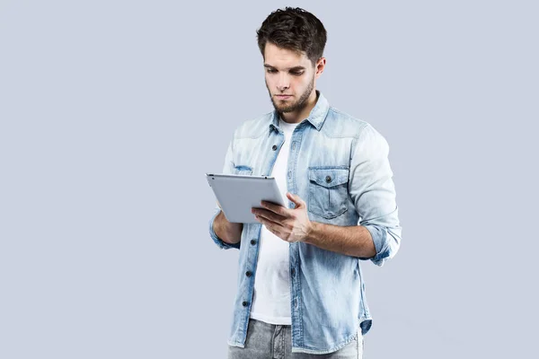 Bonito jovem usando seu tablet digital sobre fundo cinza — Fotografia de Stock
