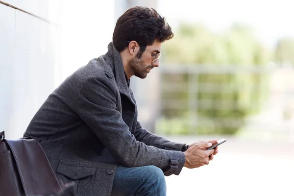 Jeune homme moderne utilisant son téléphone portable dans la rue . — Photo