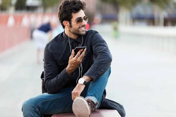 Jeune homme moderne parlant au téléphone les mains libres dans la rue . — Photo