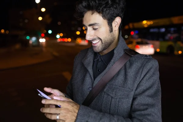 Współczesny człowiek młody za pomocą swojego telefonu komórkowego na ulicy w nocy. — Zdjęcie stockowe