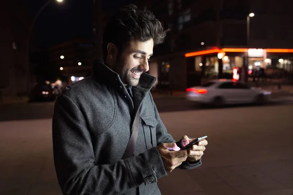 Современный молодой человек использует свой мобильный телефон на улице ночью . — стоковое фото