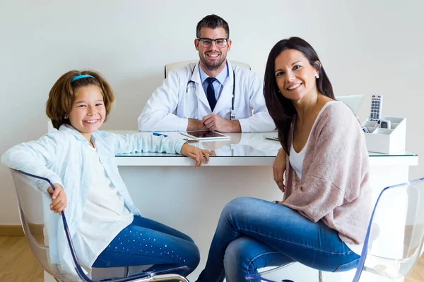 Mother and daughter with male doctor looking at camera in the office.