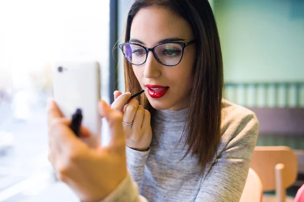 Красивая молодая женщина делает макияж с помощью помады и мобильного телефона . — стоковое фото