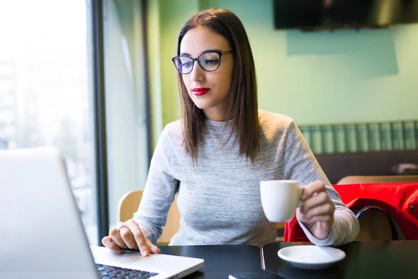 Schöne junge Frau trinkt Kaffee, während sie ihren Laptop im Café benutzt. — Stockfoto