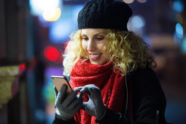 Mooie jonge vrouw met behulp van haar mobiele telefoon in de straat in de nacht. — Stockfoto