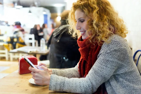 Όμορφη νεαρή γυναίκα χρησιμοποιώντας το κινητό τηλέφωνο στο κατάστημα καφέ. — Φωτογραφία Αρχείου