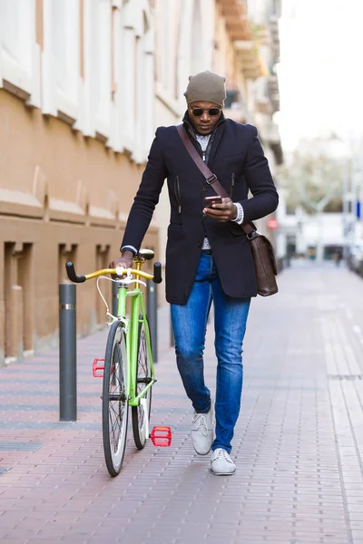 Beau jeune homme utilisant téléphone portable et vélo à engrenages fixes dans la rue . — Photo