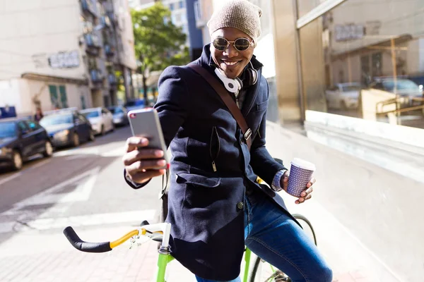 Hombre joven guapo usando el teléfono móvil y la bicicleta de engranaje fijo en la calle . — Foto de Stock