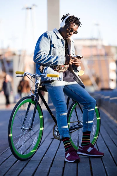 Beau jeune homme utilisant téléphone portable et vélo à engrenages fixes dans la rue . — Photo