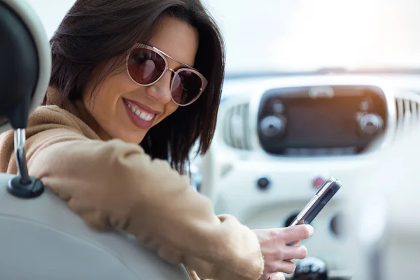 Krásná mladá žena pomocí svého mobilního telefonu v autě. — Stock fotografie