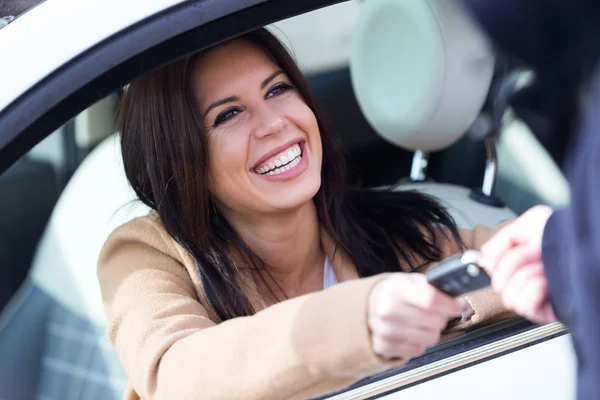 Empleado de la agencia de alquiler de coches dando llaves de coche a hermosa mujer joven . — Foto de Stock