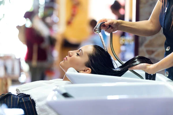 Hermosa mujer joven lava el cabello en un salón de belleza . — Foto de Stock