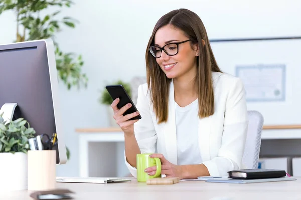 Ung affärskvinna med sin mobiltelefon på kontoret. — Stockfoto