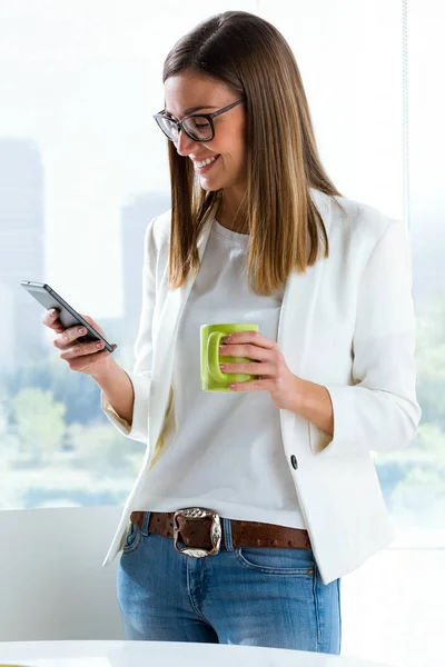 Jonge zakenvrouw met behulp van haar mobiele telefoon in het kantoor. — Stockfoto