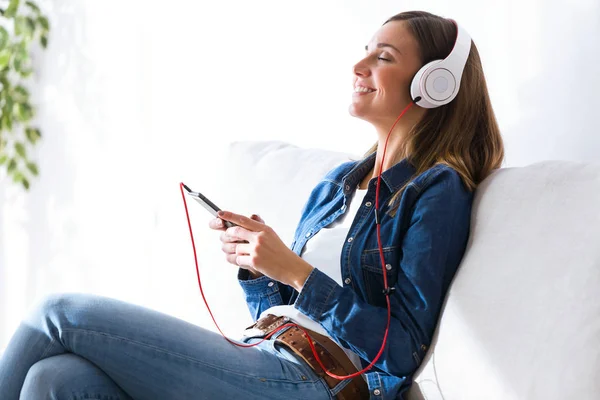 Mulher bonita ouvindo música com telefone celular em casa . — Fotografia de Stock
