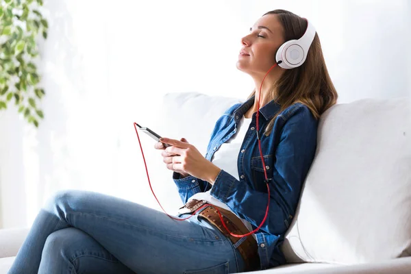 Mooie jonge vrouw, luisteren naar muziek met mobiele telefoon thuis. — Stockfoto