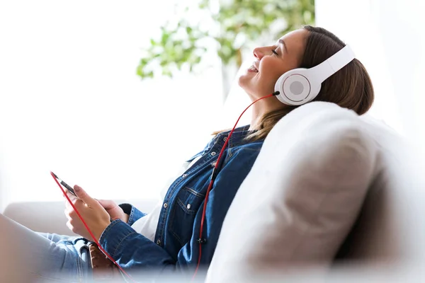Schöne junge Frau hört zu Hause Musik mit Handy. — Stockfoto