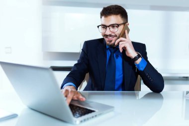 Dizüstü bilgisayar ve cep telefonu ofisteki çalımakta yakışıklı genç.