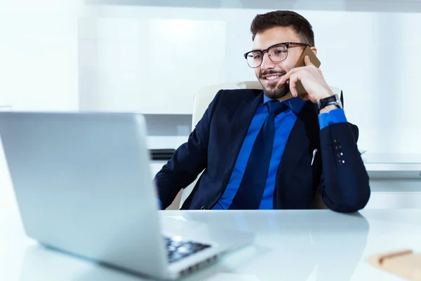 Jovem bonito trabalhando com laptop e telefone celular no escritório . — Fotografia de Stock