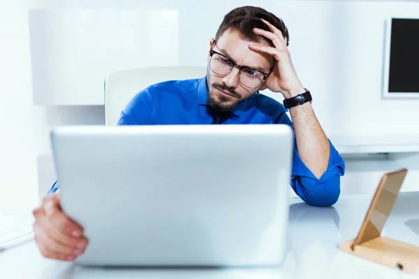 Bonito jovem empresário estressado enquanto trabalhava com laptop no escritório . — Fotografia de Stock